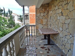Un balcon avec un mur en pierre, un sol carrelé et une table recouverte d’une nappe.
