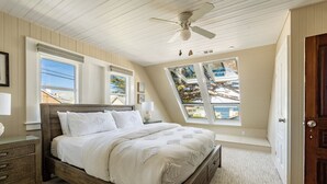 Un dormitorio con una cama de madera, ventilador de techo y grandes ventanales que ofrecen vistas al exterior.