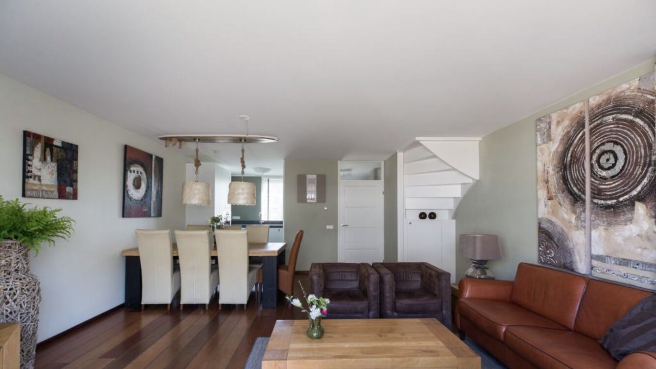 Een moderne woonkamer met een eetgedeelte, een bruine leren bank en een groot abstract schilderij.