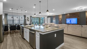 Une cuisine moderne dotée d'un îlot central, d'un coin repas avec des chaises et d'un salon avec un canapé et une télévision.
