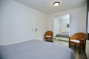 Une chambre à coucher avec un lit, deux fauteuils en osier, une armoire et un miroir.