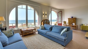 Una sala de estar con un amplio ventanal con vistas al mar, un sofá azul y una mesa de centro de madera.