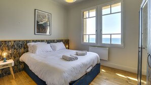 Un dormitorio con una cama, una mesita de noche, una lámpara de pared, una ventana y una puerta.