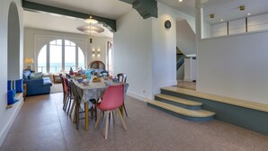 Un comedor con una mesa dispuesta para cuatro personas, rodeada de sillas. Se ve una escalera que sube a un nivel superior.