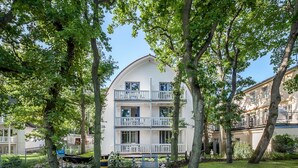 Ein zweistöckiges Gebäude mit weißer Fassade, Balkonen und einem Gartenweg, der zum Eingang führt.