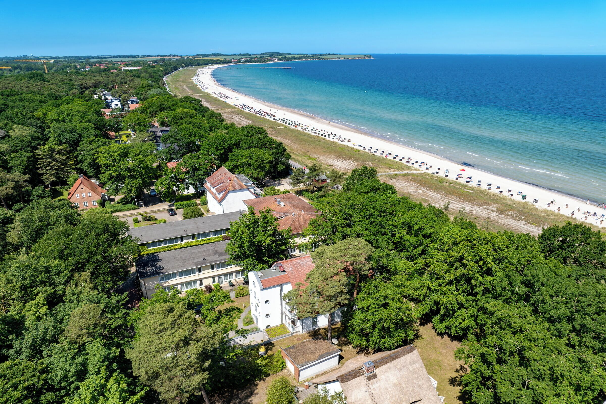 Vue aérienne d’une zone côtière avec une plage, des bâtiments et une végétation luxuriante.