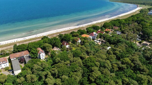 Luftaufnahme einer Küstenlandschaft mit Strand, Häusern und dichter Vegetation.