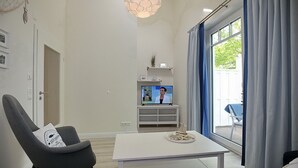 Uma sala de estar moderna com uma televisão, uma mesa de centro branca e uma poltrona cinzenta.