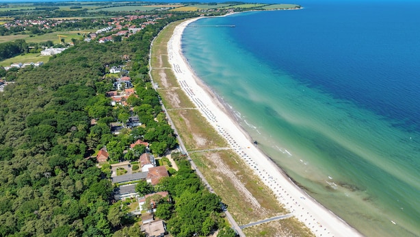 Vista aérea de un pueblo costero con una playa extensa, abundante vegetación y edificios residenciales.