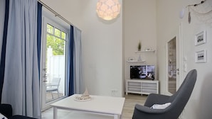 Una sala de estar moderna con una mesa de centro blanca, un sillón gris y un televisor sobre un mueble blanco.