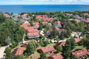 An aerial view of a residential area with red-roofed houses, surrounded by greenery and a body of water in the background. - Papillon Wohnung 15-1 (Ostseebad Boltenhagen)