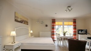 Ein Schlafzimmer mit einem Bett, Nachttischen, einem Schreibtisch, einem Sessel, einem Fernseher und einem Fenster mit Vorhängen.