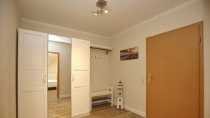 Ein Zimmer mit Holzboden, einer weißen Tür, einem Holzschrank, einem kleinen weißen Regal und einem an der Wand hängenden Bild.