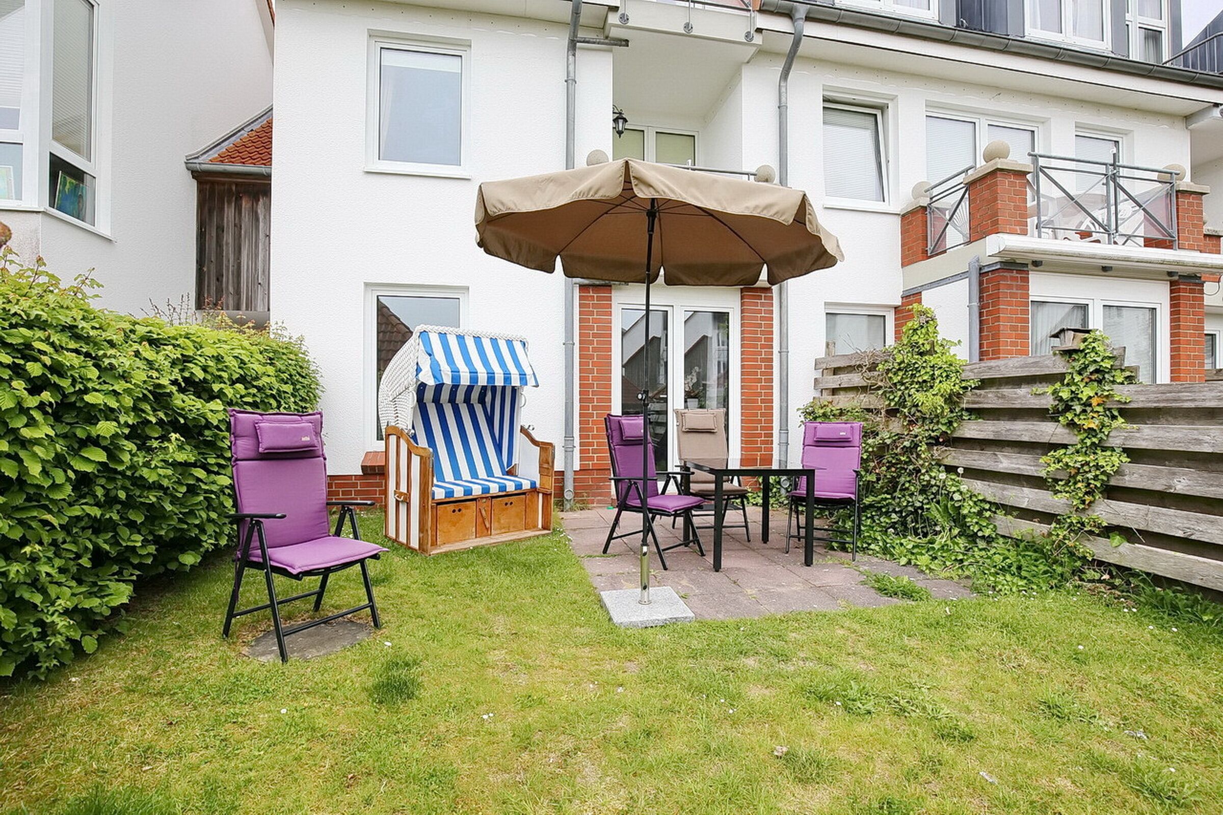 Een patio met een tafel en stoelen, een gestreepte strandstoel en een grote parasol.