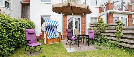 Een patio met een tafel en stoelen, een gestreepte strandstoel en een grote parasol.