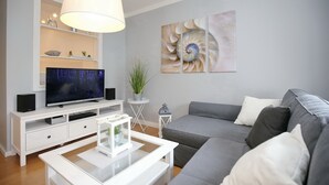 A modern living room with a grey sofa, a white coffee table, a flat-screen TV on a white entertainment unit, and a large white pendant light.