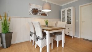 A dining area with a wooden table and white chairs, a hanging lamp, a cabinet with glass doors, and a potted plant.