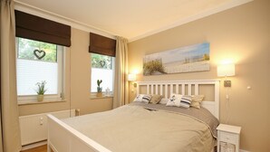 A bedroom with a large bed, a nightstand with a lamp, a window with curtains, and a painting on the wall.