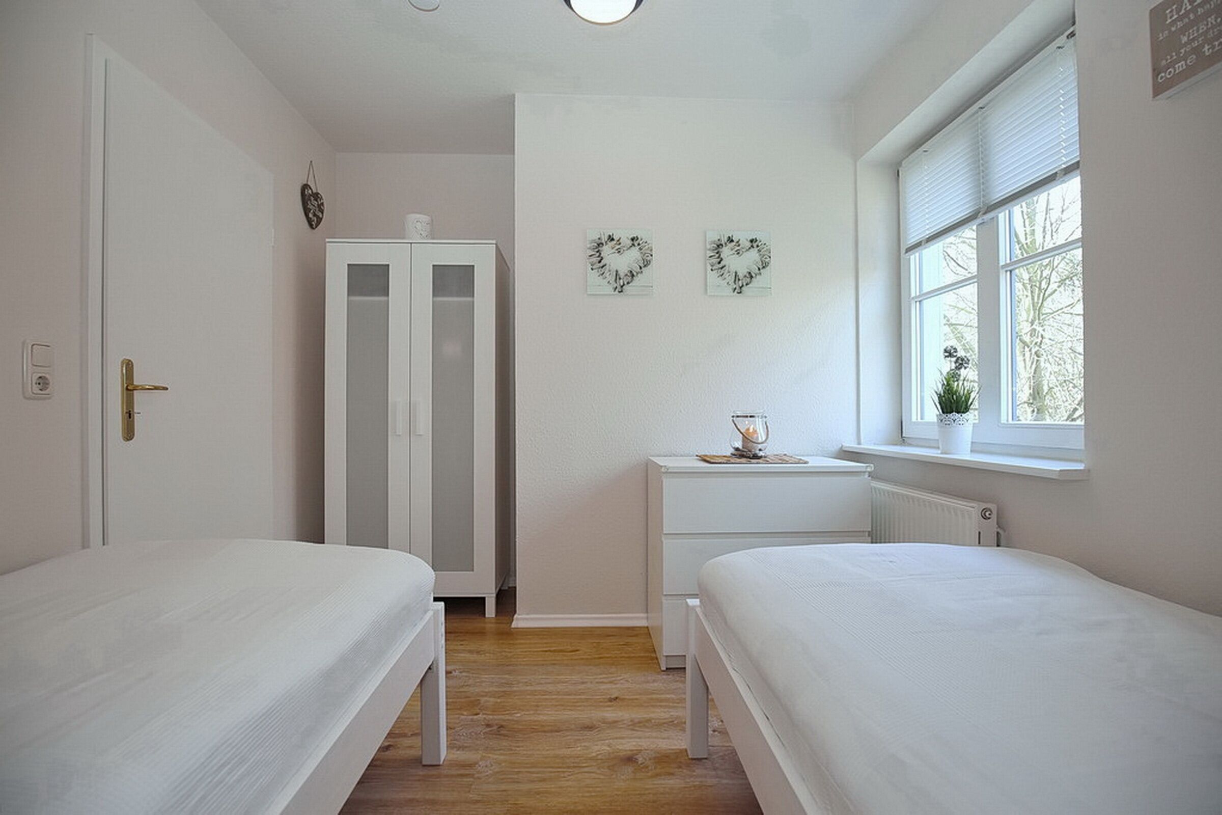 A bedroom with two beds, a wardrobe, a bedside table, and a window with a view.