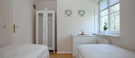 A bedroom with two beds, a wardrobe, a bedside table, and a window with a view.