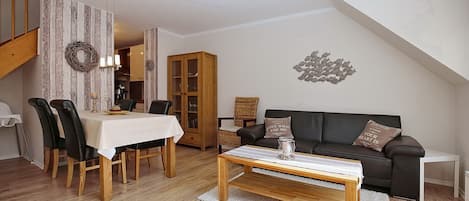 Een gezellige woonkamer met een eethoek, een zwarte leren bank, houten meubels en een decoratief kunstwerk aan de muur.