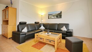 Ein Wohnzimmer mit Ecksofa, Glastisch, Holzschrank und Wandlampe.
