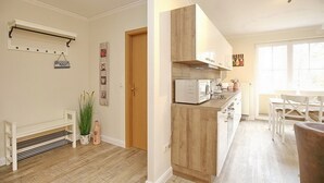 Moderni keittiö, jossa on puiset kaapit, mikroaaltouuni sekä ruokailutila, jossa on pöytä ja tuolit.