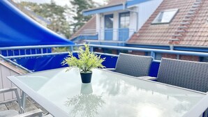 Une table à plateau en verre, une plante en pot, des chaises en osier grises et, au fond, une marquise bleue.