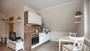 Een compacte keuken met witte kastjes, een magnetron, een koffiezetapparaat en een kleine eethoek met een tafel en stoelen.