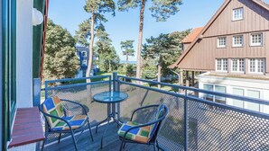 Een balkon met twee stoelen en een kleine tafel, met uitzicht op een bebost gebied en een gebouw met een bruin dak.