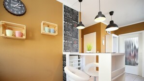 Une cuisine moderne avec un plan de travail blanc, des luminaires suspendus et des étagères en bois où sont posées des tasses.