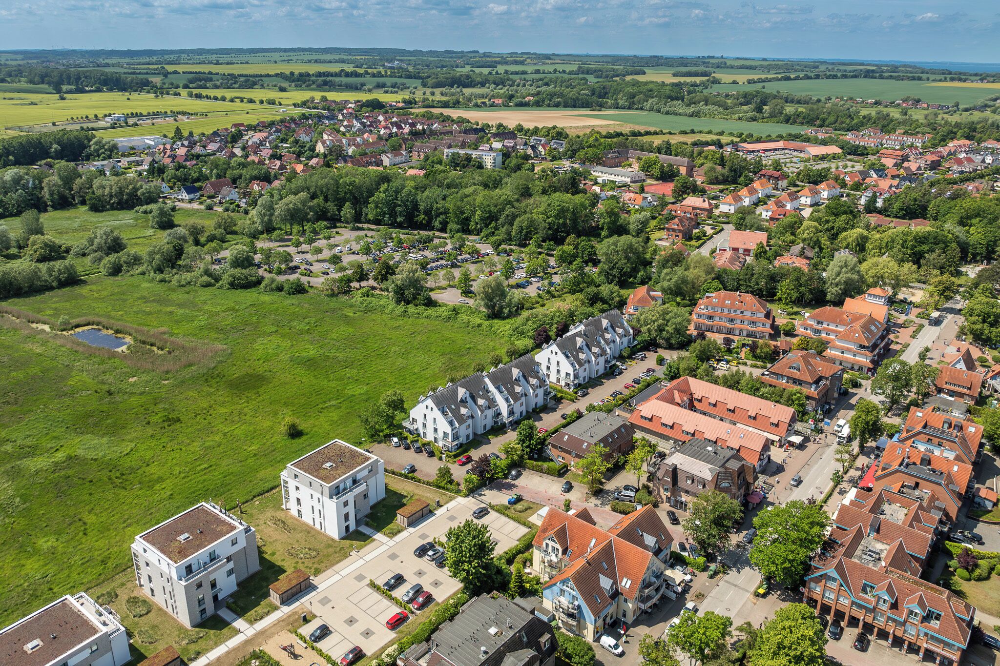 An aerial view of a residential area with houses, green fields, and a parking lot.