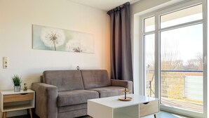 Una sala de estar moderna con un sofá gris, una mesita auxiliar blanca y una mesa de centro. Hay un ventanal con vistas al exterior.