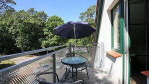 Un balcón con mesa y sillas, una sombrilla azul y vistas a árboles.