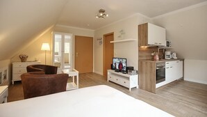Una habitación compacta y bien iluminada con una cama, televisor, kitchenette y un pequeño rincón de descanso.