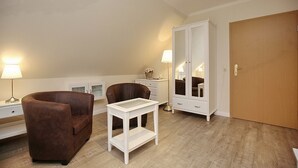 Una habitación con una silla de cuero marrón, una mesita auxiliar blanca, un mueble espejo grande y una puerta de madera.