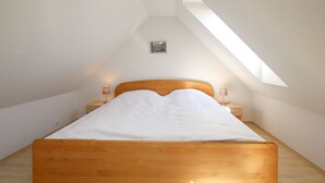 Een slaapkamer met een houten bed, een nachtkastje, een lamp en een dakvenster.