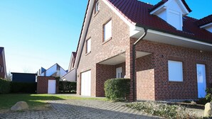 Een huis van baksteen met een rood dak, een garage en een verharde oprit.