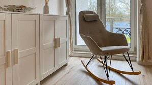 A room with a white wardrobe, a rocking chair, and a view of the outdoors through a glass door.