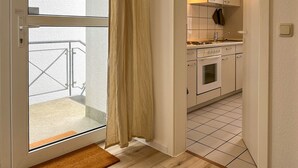 A narrow kitchen with white cabinets, a stove, and a window with a curtain.