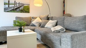 A modern living room with a grey patterned sofa, a white side table with a plant, a floor lamp, and a bookshelf against the wall.