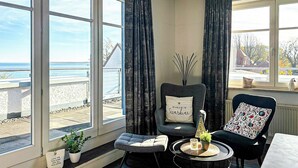 Ein Zimmer mit Meerblick, ausgestattet mit einem Sessel, einem Kissen, einem kleinen Tisch mit Kerze und einem Blumentopf.