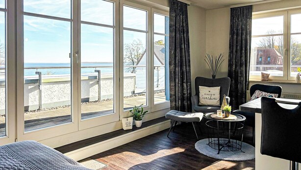 Ein Zimmer mit großen Fenstern, einer Couch, einem Esstisch und einem Stuhl.