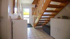 Una cocina con una escalera de madera, un refrigerador, armarios y un perchero.