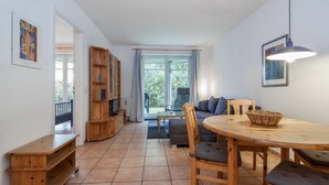 A cozy living area with a wooden dining table, chairs, a sofa, and a bookshelf. - Dünenblick Wohnung 19 (Ostseebad Boltenhagen)