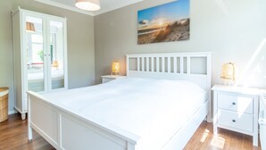 Une chambre à coucher avec un lit blanc, une table de chevet avec une lampe et un tableau accroché au mur.