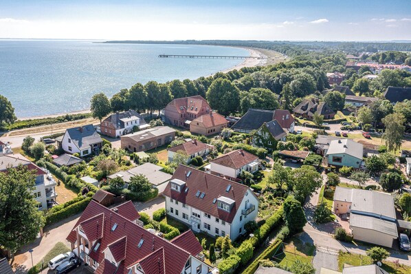 An aerial view of a residential area with houses, a pier extending into the water, and a beach in the background.
