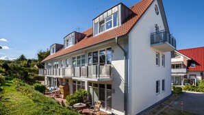 Une maison à deux étages dotée d’un balcon, de grandes fenêtres et d’un toit recouvert de tuiles rouges.