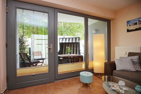 Ein Wohnzimmer mit Glastür zu einem Außenbereich, einem Sofa, einem Glastisch und einer Lampe.