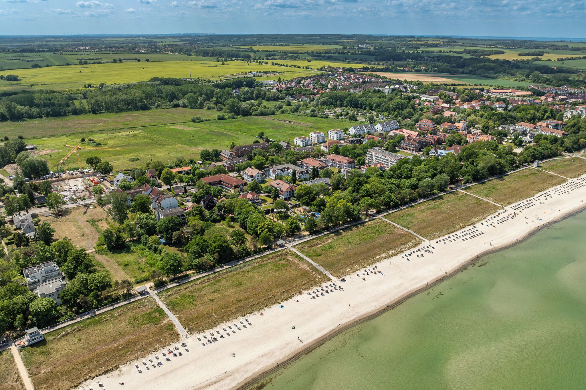 Vista aérea de un pueblo costero con playa, casas y campos verdes.